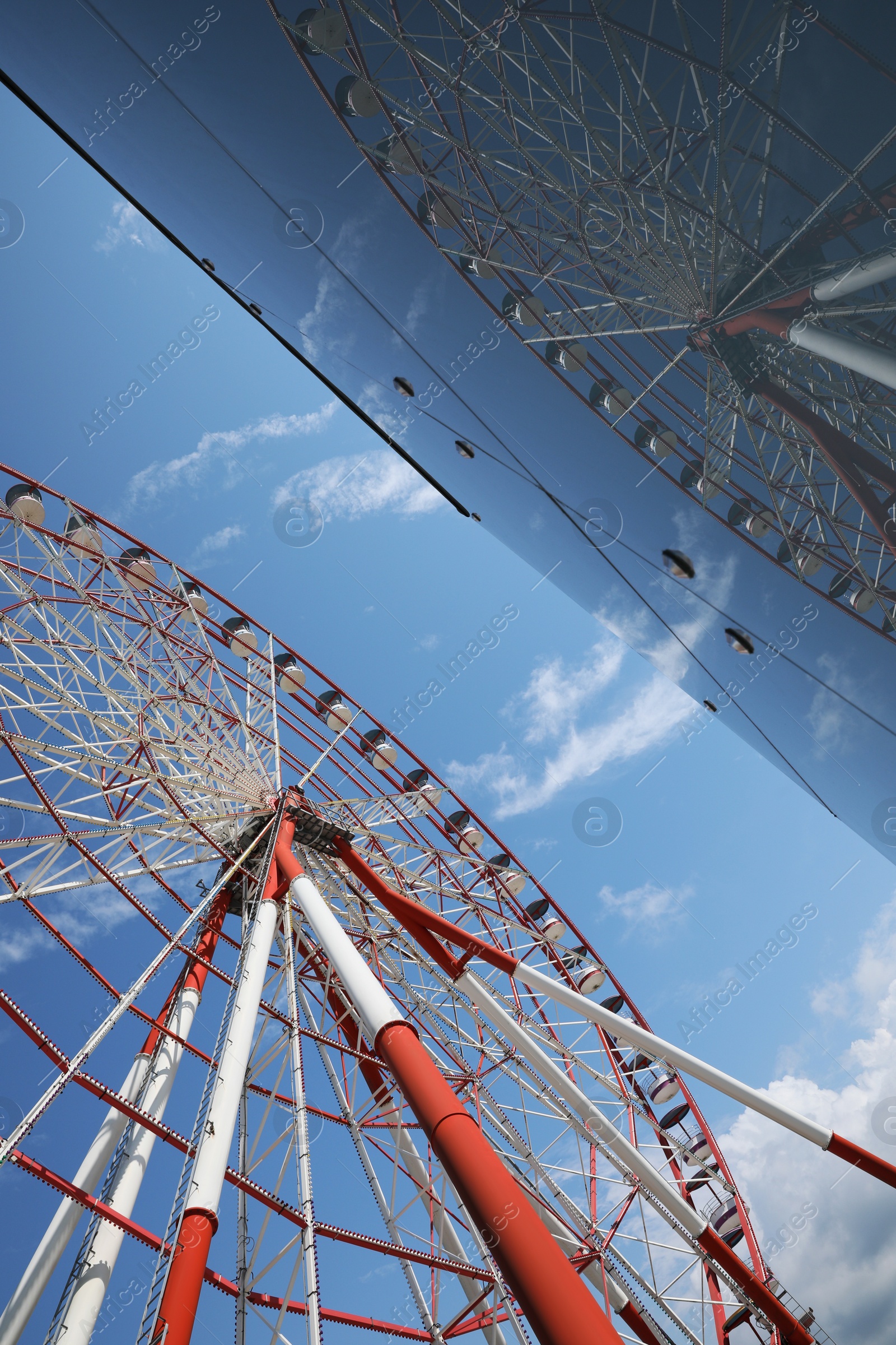 Photo of Beautiful large Ferris wheel near building against blue sky, low angle view