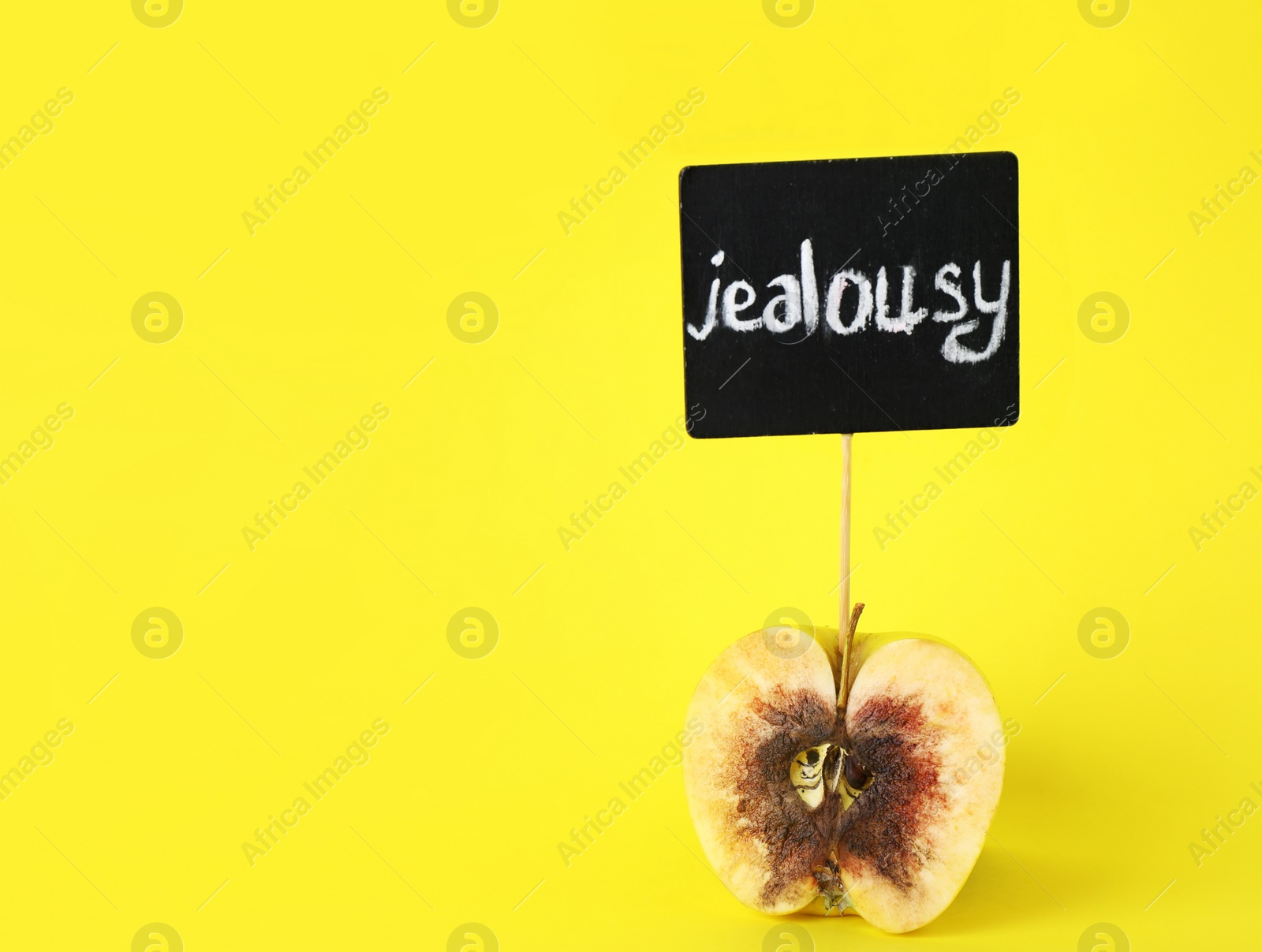 Photo of Rotten apple with JEALOUSY sign on yellow background. Space for text