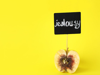 Photo of Rotten apple with JEALOUSY sign on yellow background. Space for text