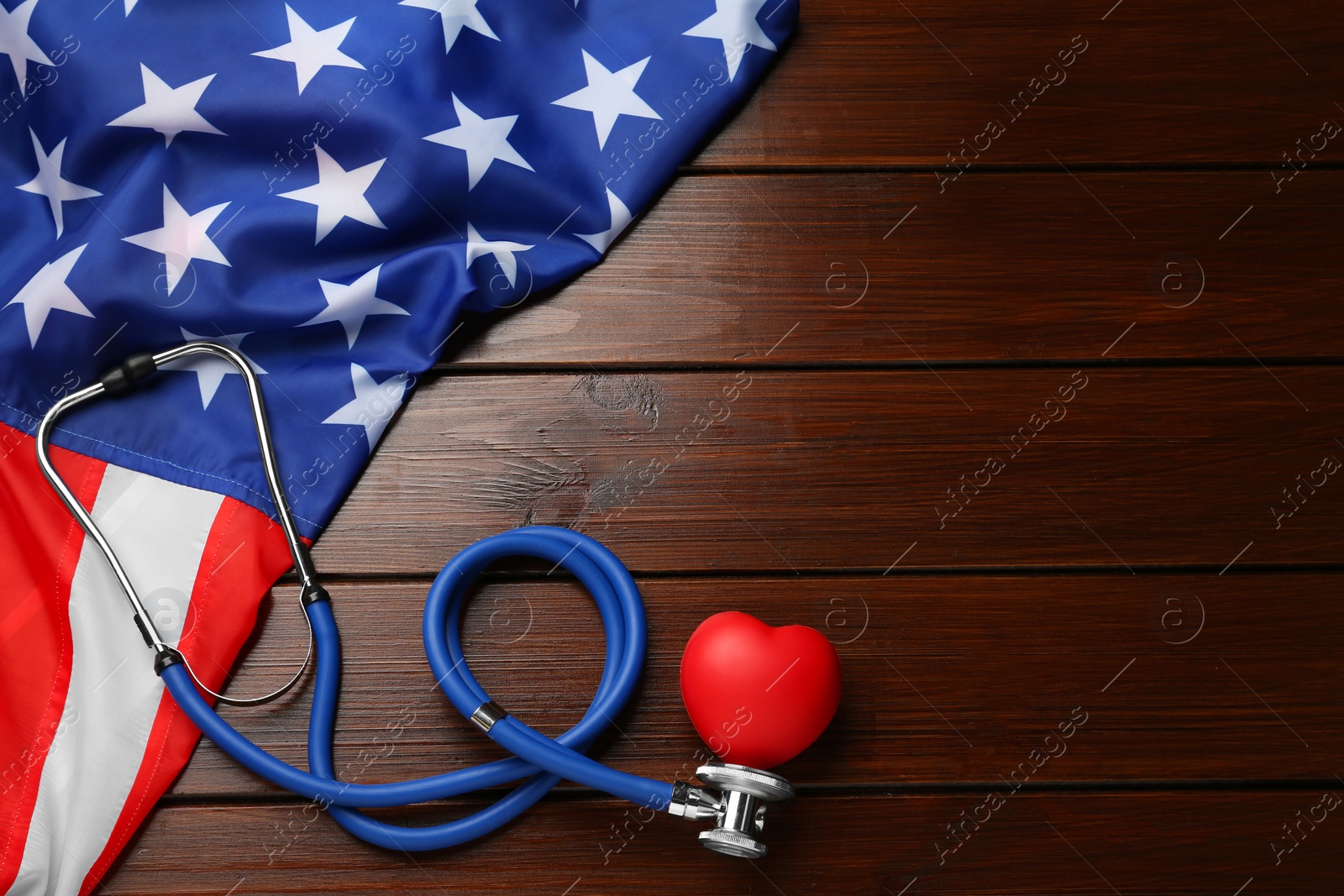 Photo of Stethoscope, red heart and American flag on wooden table, flat lay. Space for text