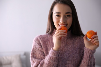 Happy young woman with fresh ripe tangerines at home