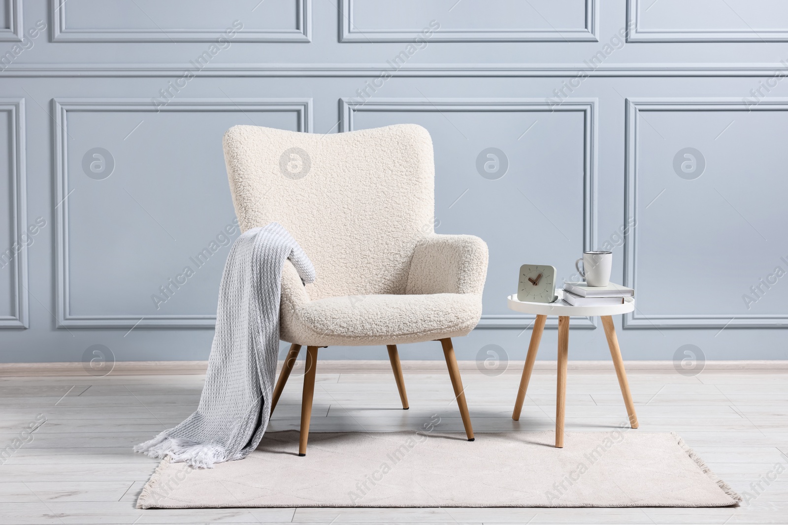 Photo of Comfortable armchair with blanket and side table indoors