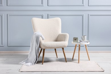 Photo of Comfortable armchair with blanket and side table indoors