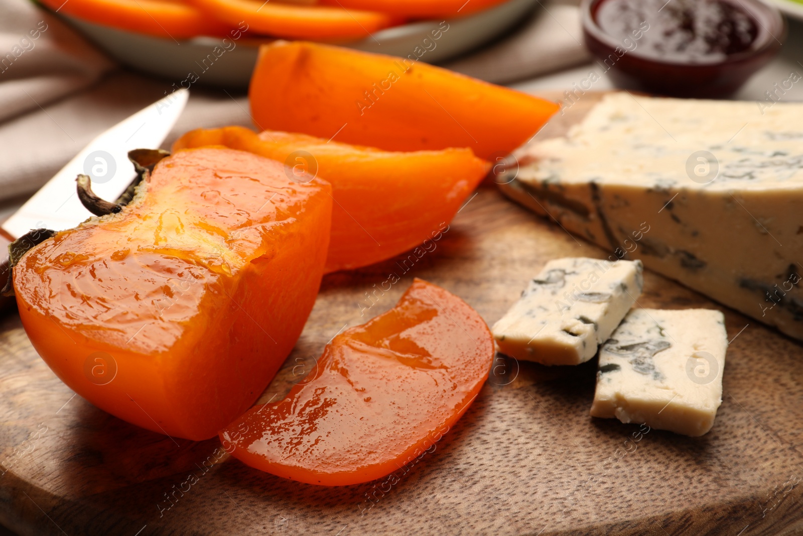 Photo of Tasty sliced persimmon and blue cheese on wooden board, closeup