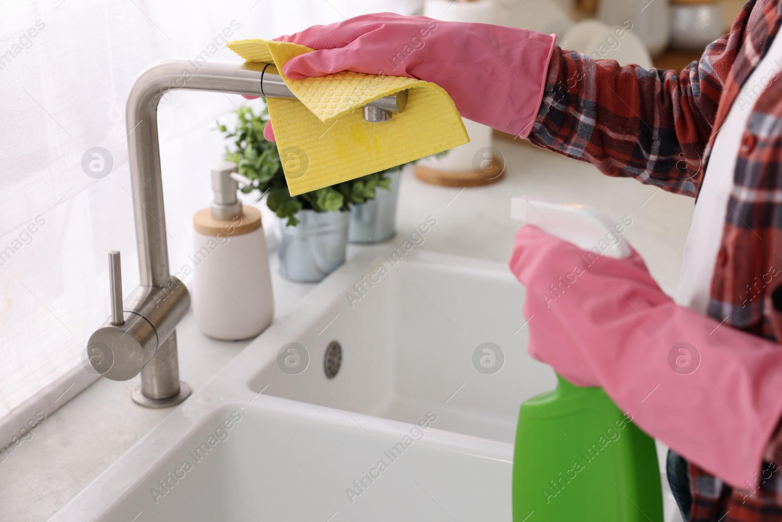 Photo of Woman with spray bottle and microfiber cloth cleaning water tap in kitchen, closeup
