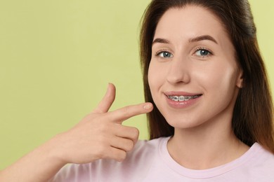 Portrait of smiling woman pointing at her dental braces on light green background. Space for text