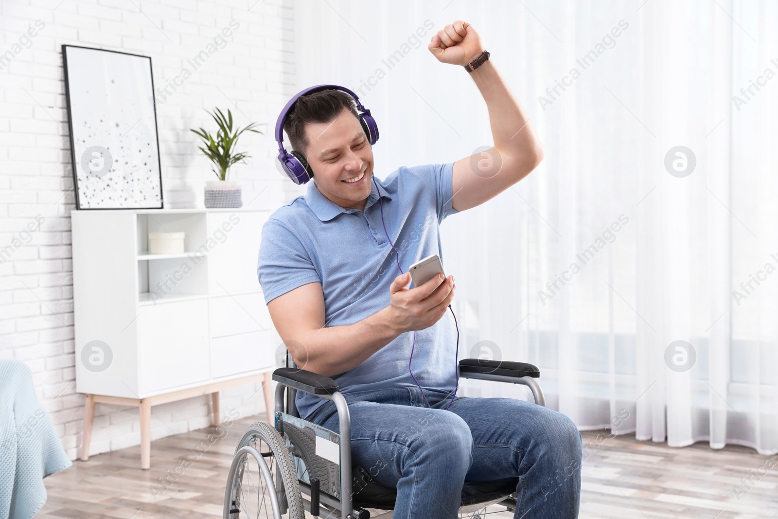 Photo of Happy man with headphones and mobile device in wheelchair at home