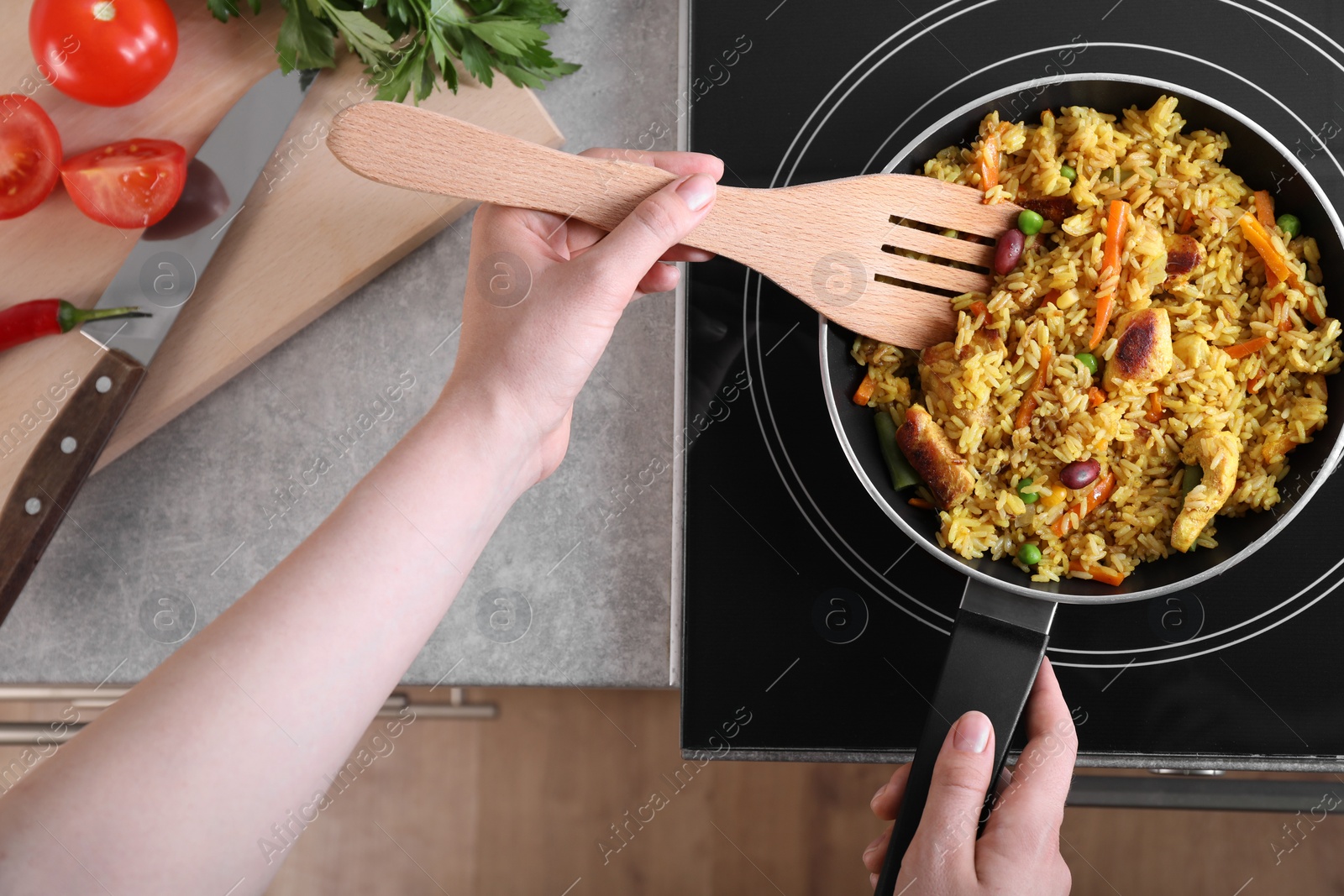 Photo of Woman frying rice with meat and vegetables on induction stove in kitchen, closeup