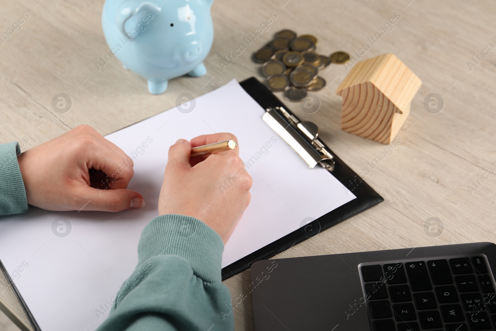 Photo of Woman planning budget, closeup. House model, coins and piggy bank on wooden table