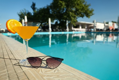 Photo of Tasty refreshing cocktail and sunglasses on edge of swimming pool. Party items