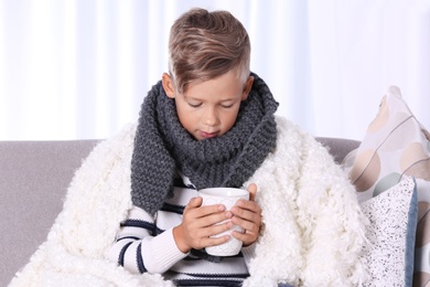 Photo of Ill little boy with cup of hot tea for cough on sofa