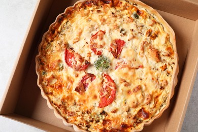 Tasty quiche with tomatoes and cheese in open box on light table, top view