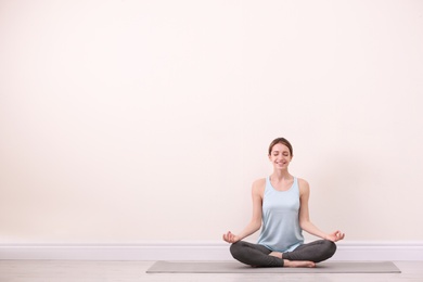 Photo of Young woman meditating near light wall, space for text. Zen concept