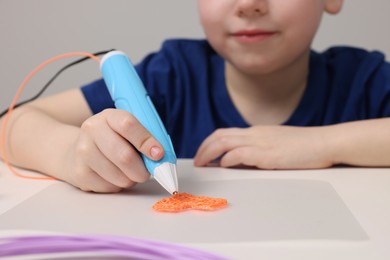 Photo of Boy drawing with stylish 3D pen at white table, closeup
