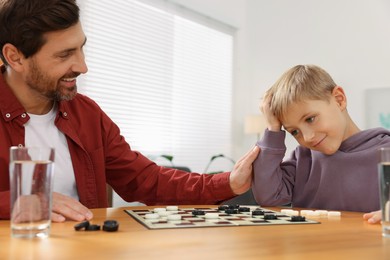 Photo of Father cheering his son while they playing checkers in room