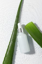 Bottle of cosmetic product and aloe leaves in water on white background, flat lay