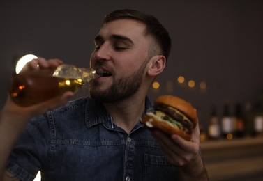 Young man with beer eating tasty burger in cafe