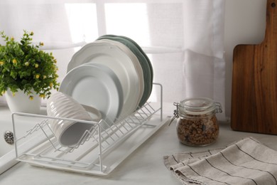 Drainer with different clean dishware and cup on light table indoors