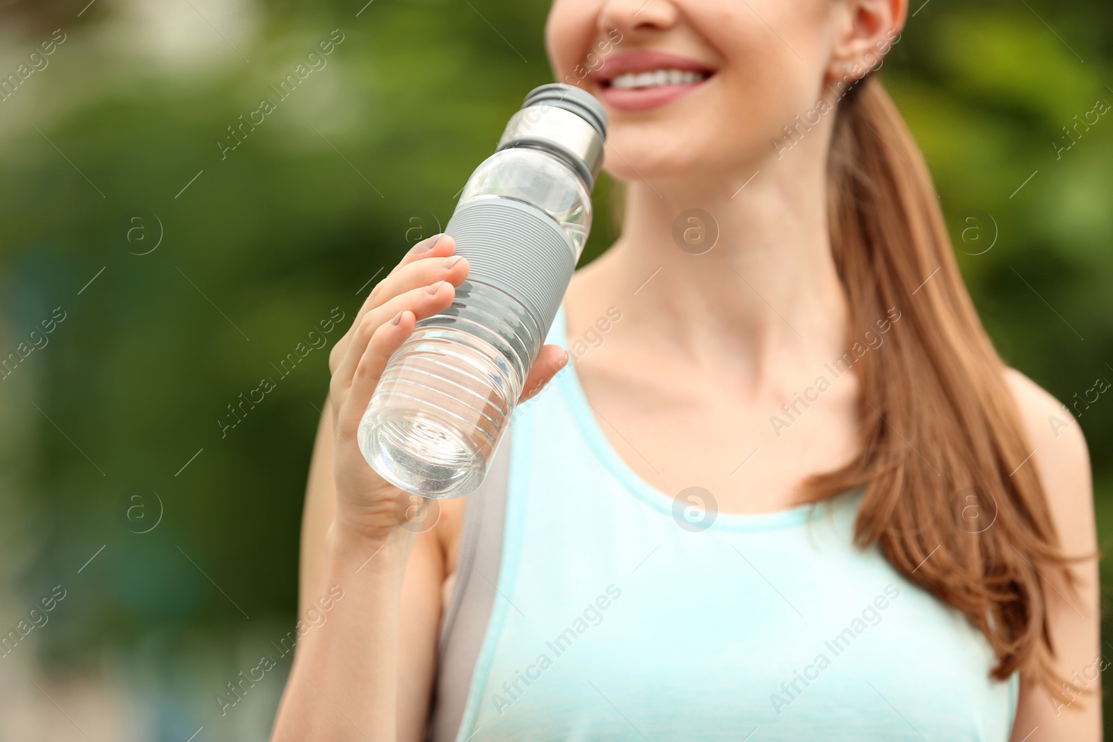 Photo of Young woman with bottle of water outdoors, closeup. Refreshing drink