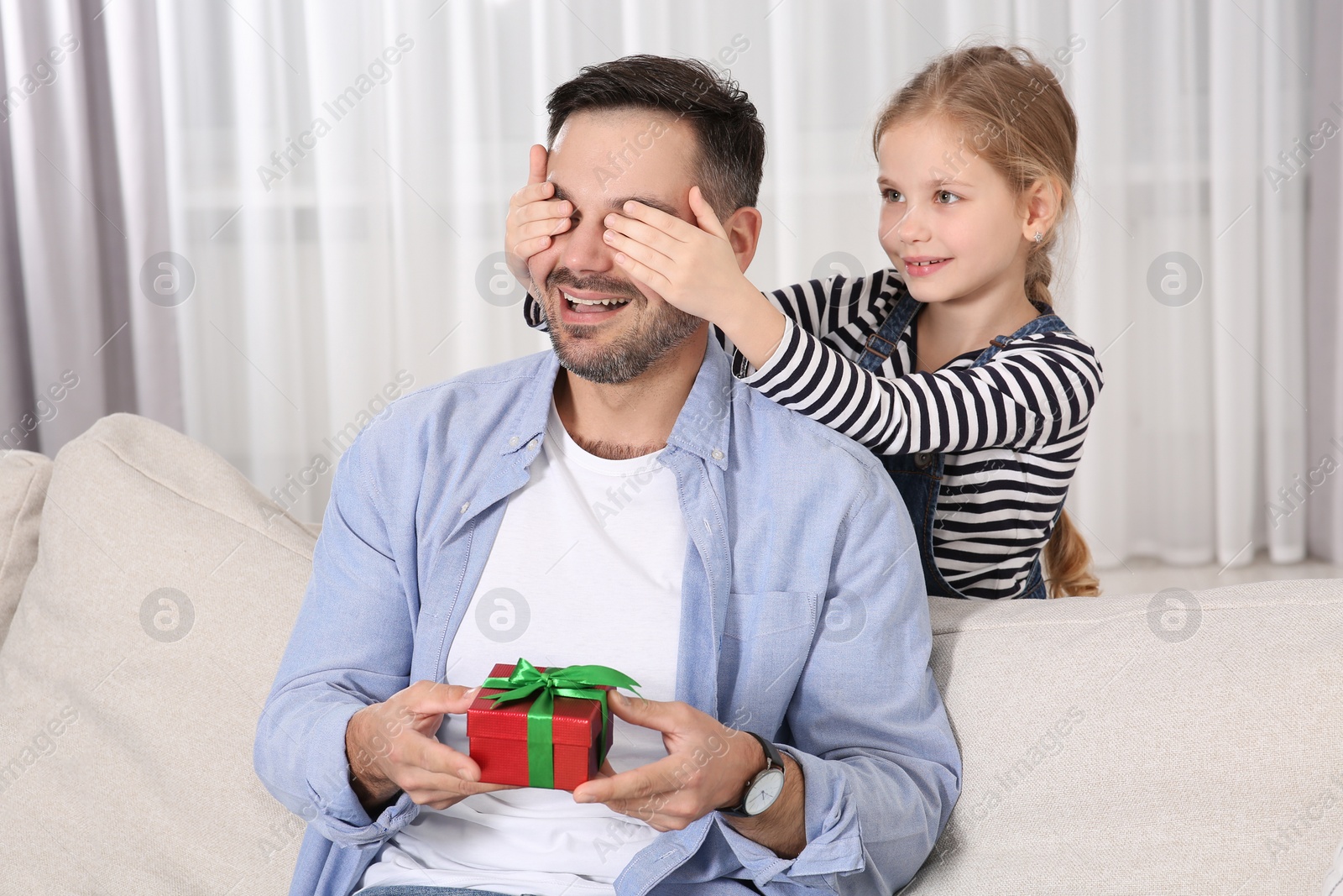 Photo of Cute little girl presenting her father with gift at home