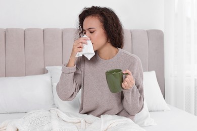 Photo of Sick African American woman with tissue and cup of drink in bed at home