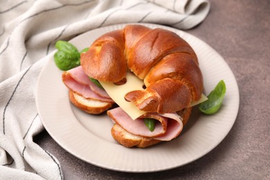 Photo of Tasty crescent roll with ham, cheese and basil on grey table, closeup