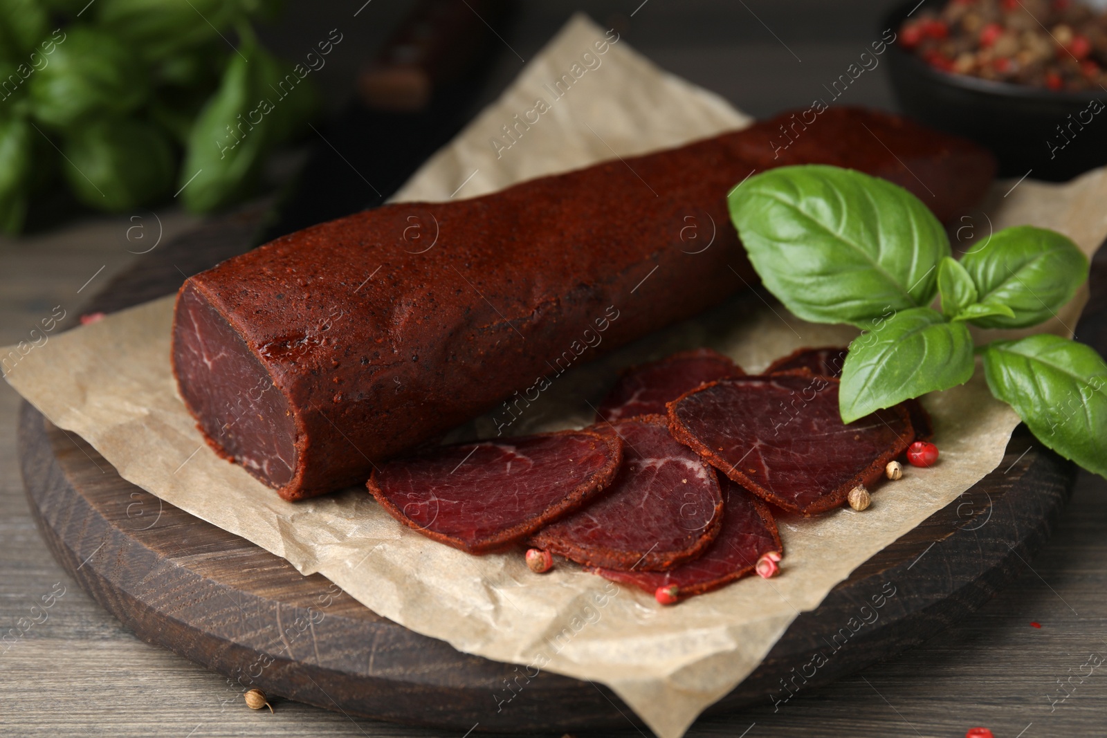 Photo of Delicious dry-cured beef basturma with basil and peppercorns on wooden table, closeup