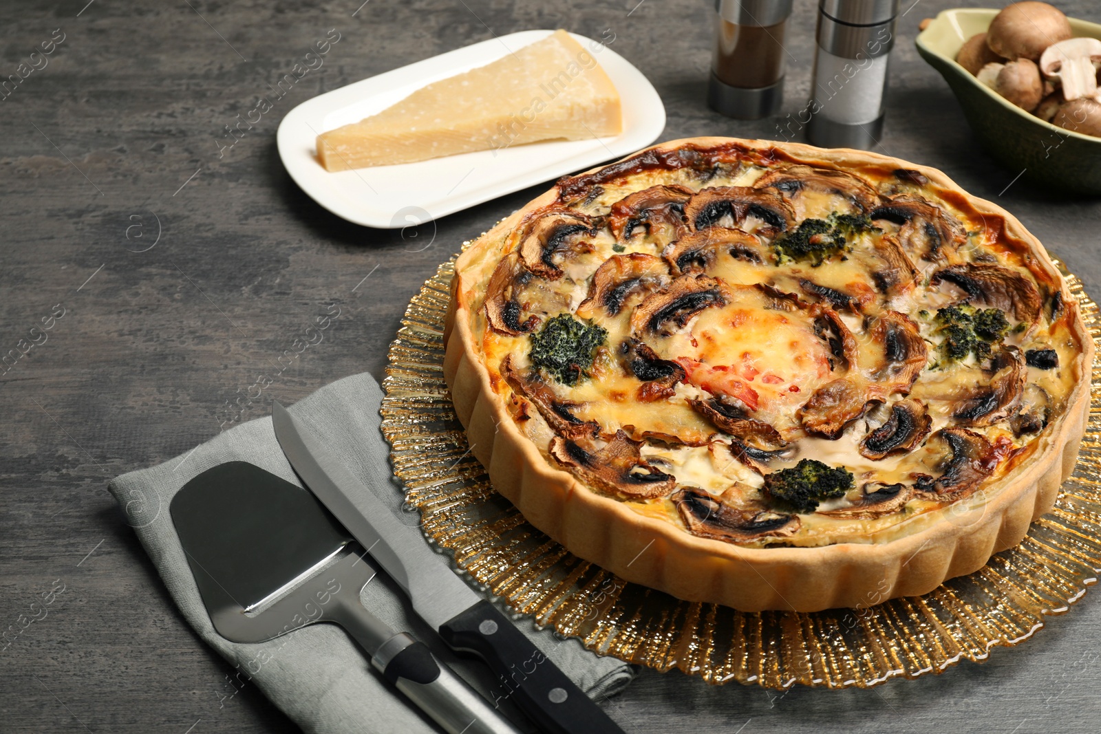 Photo of Delicious quiche with mushrooms and ingredients on dark grey table, closeup