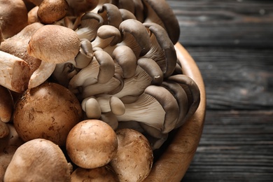 Photo of Different fresh wild mushrooms in bowl on wooden table, closeup
