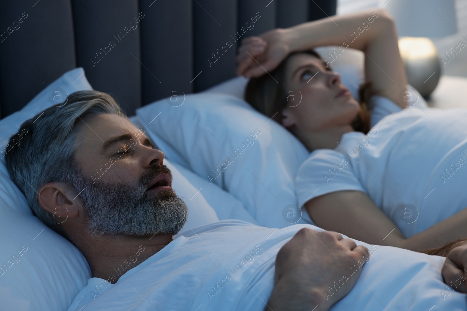 Photo of Irritated woman lying near her snoring husband in bed at home