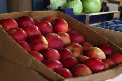 Photo of Many fresh apples in cardboard container at market