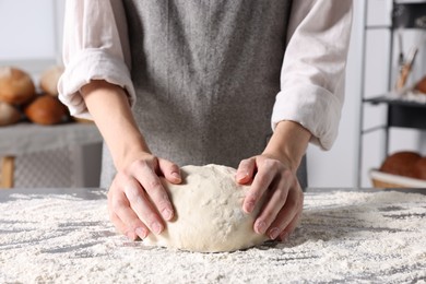 Photo of Woman kneading dough at table in kitchen, closeup