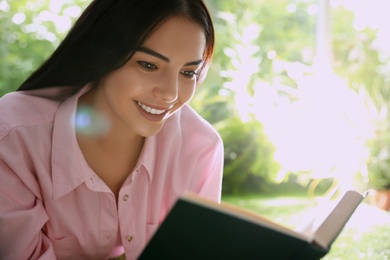 Beautiful young woman reading book in park on sunny day