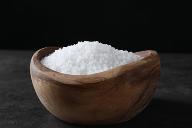 Photo of Natural salt in wooden bowl on dark grey table, closeup