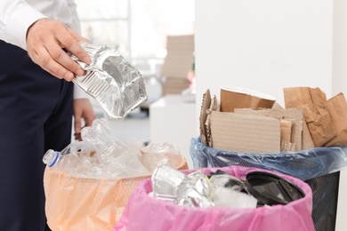 Photo of Man putting used foil container into trash bin in office, closeup. Waste recycling