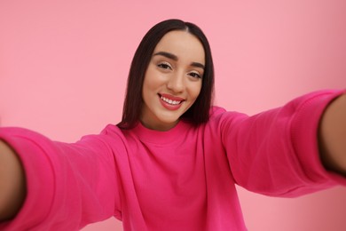 Smiling young woman taking selfie on pink background