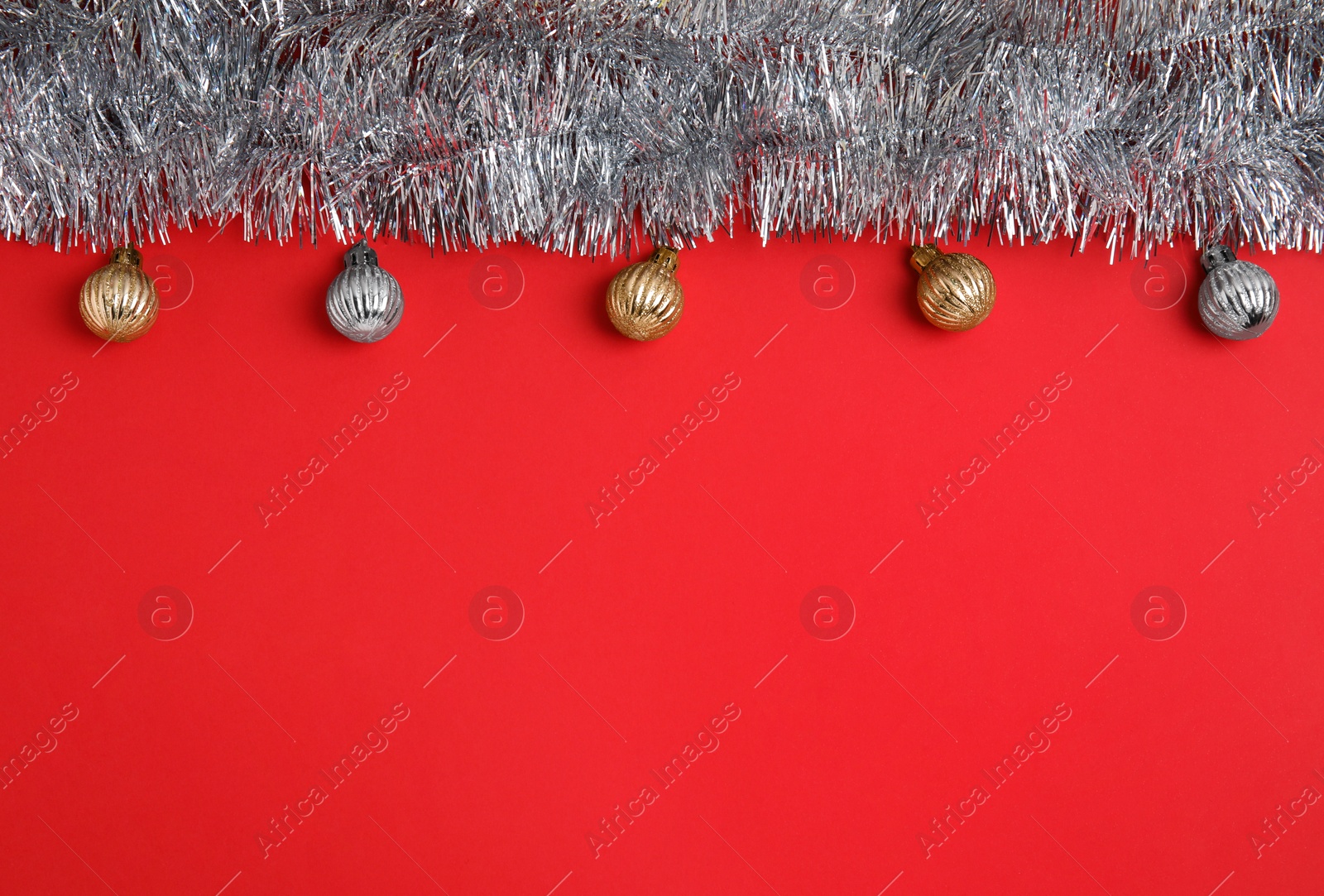 Photo of Silver tinsel and Christmas balls on red background, flat lay. Space for text