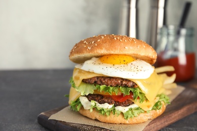 Photo of Tasty burger with fried egg on wooden board, space for text