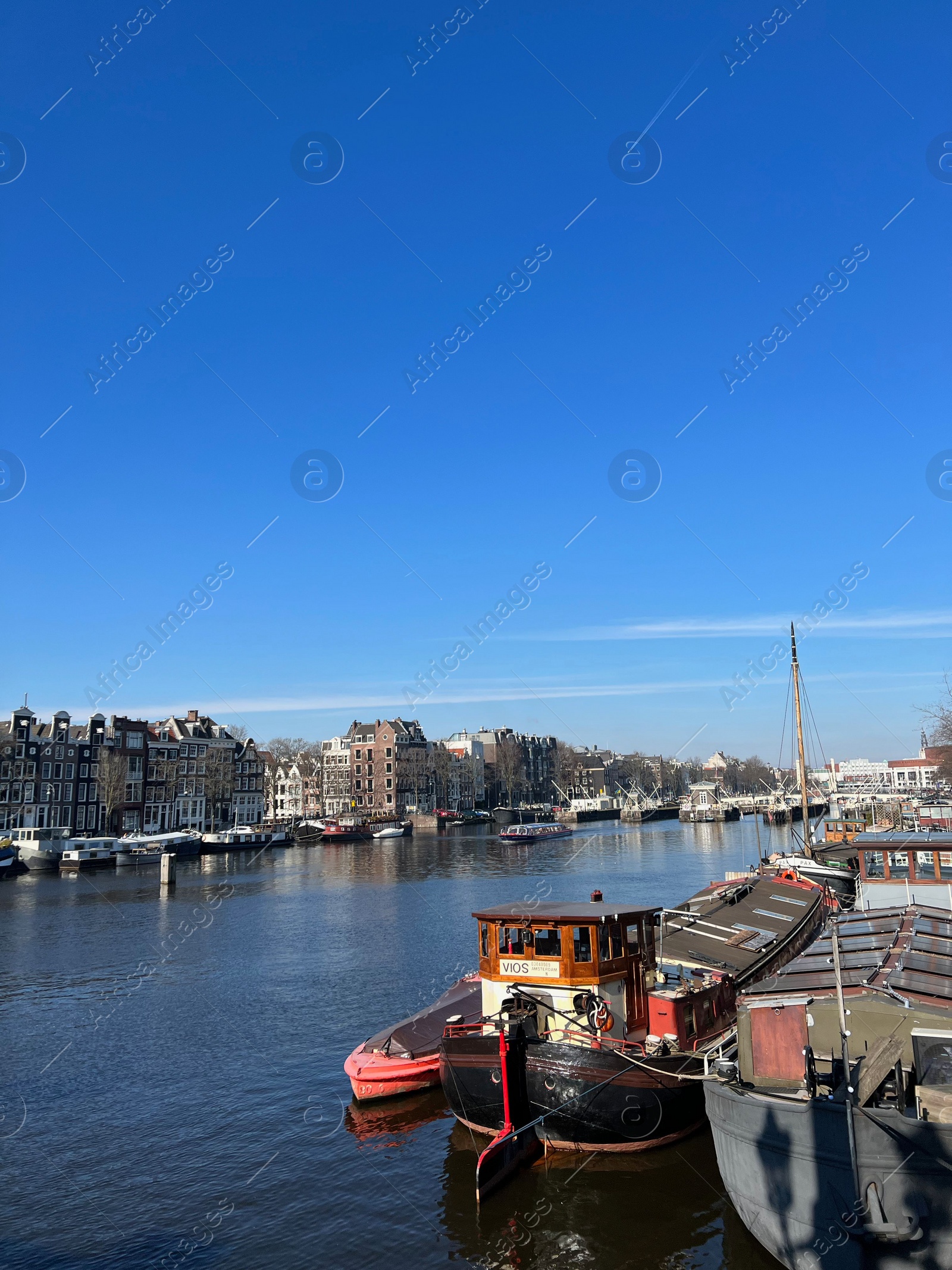 Photo of Amsterdam, Netherlands - March 01, 2023: Picturesque view of river embankment with moored boats in city under blue sky