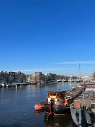 Amsterdam, Netherlands - March 01, 2023: Picturesque view of river embankment with moored boats in city under blue sky