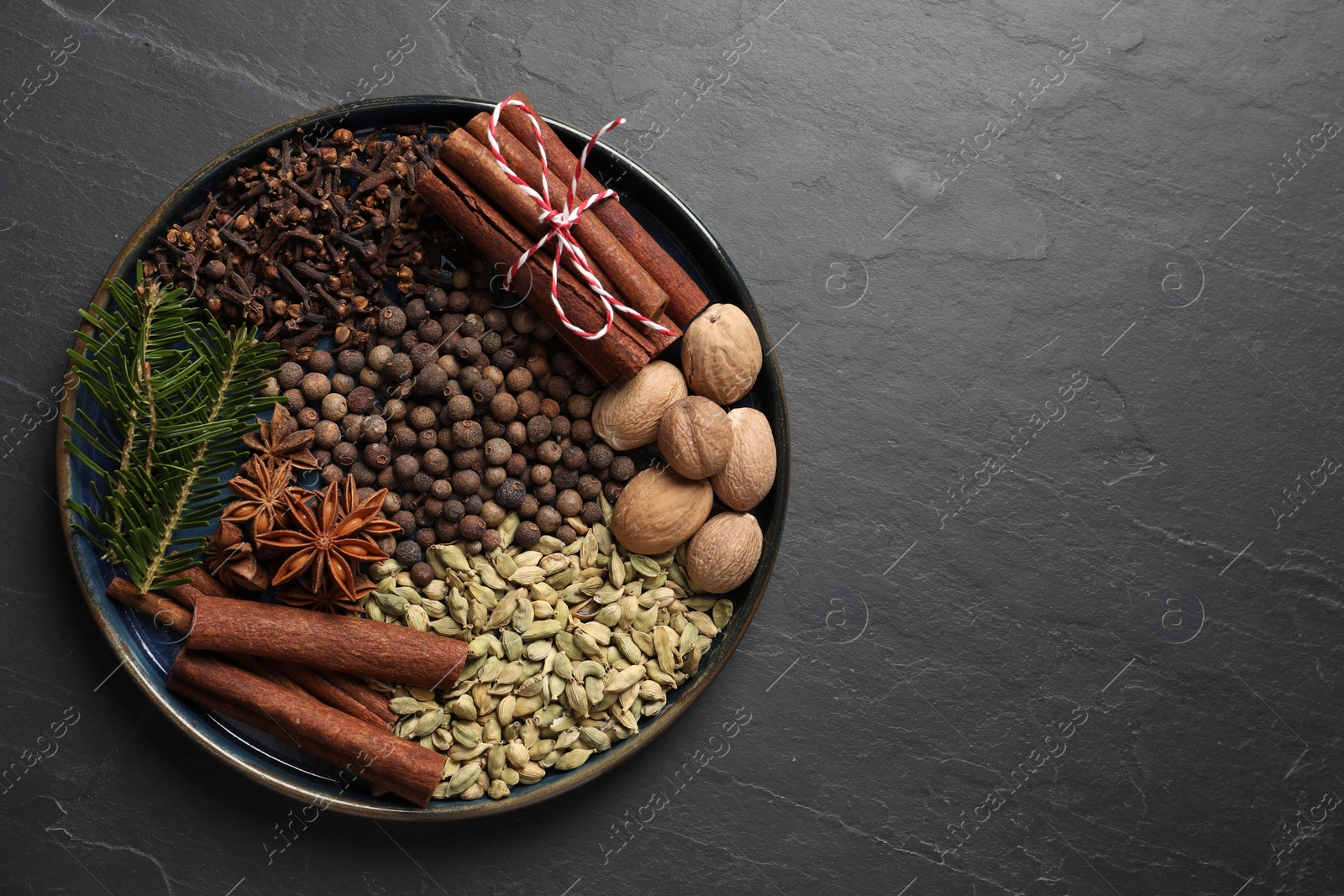 Photo of Different spices, nuts and fir branches on dark gray textured table, top view. Space for text