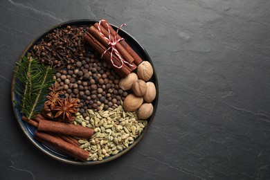 Different spices, nuts and fir branches on dark gray textured table, top view. Space for text