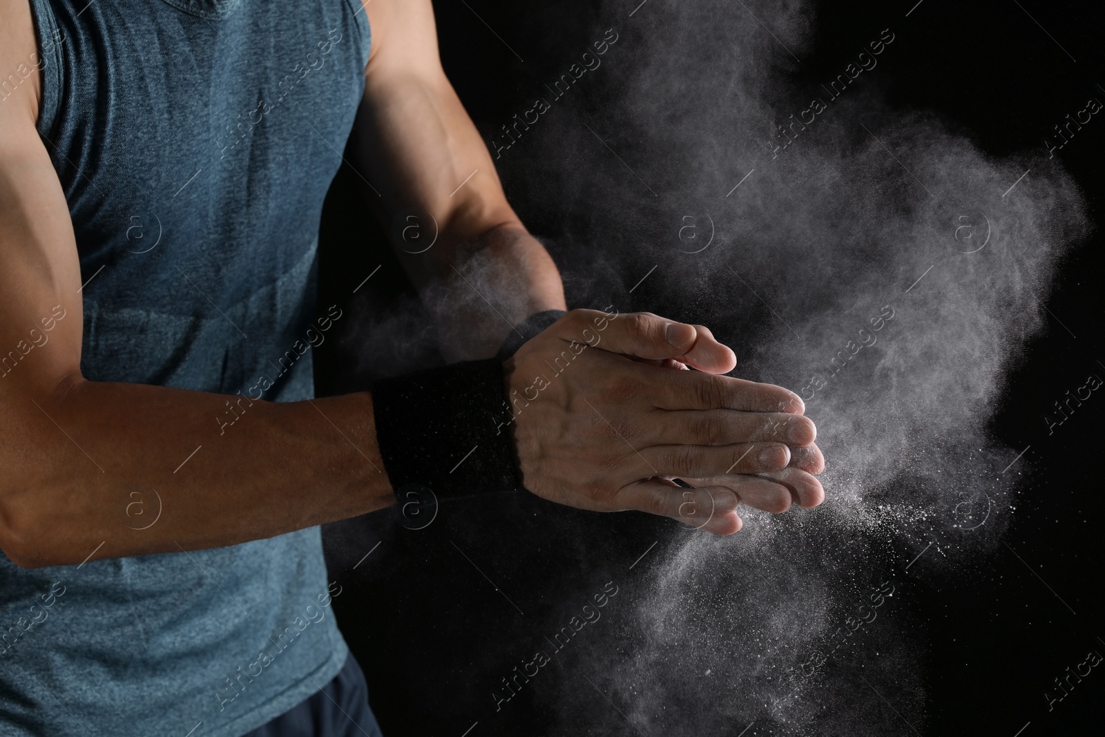 Photo of Young man applying chalk powder on hands against dark background