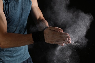 Photo of Young man applying chalk powder on hands against dark background