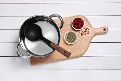 Steel pot, board, ladle and spices on white wooden table, top view