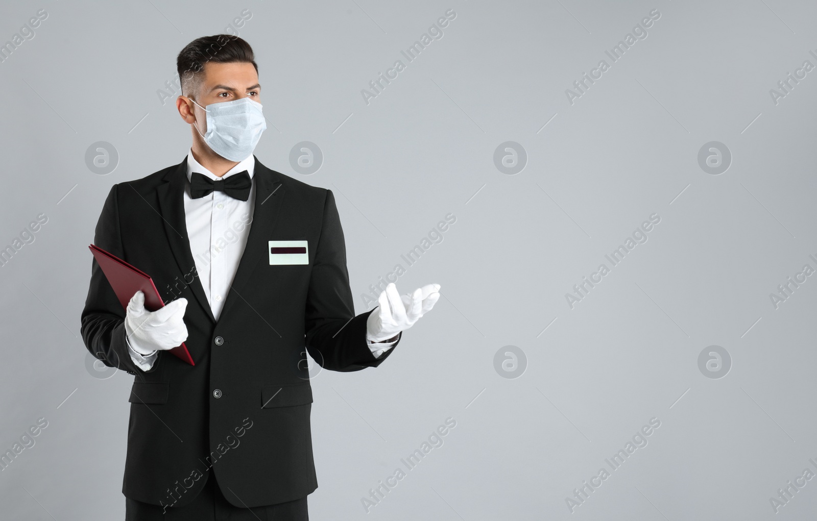 Photo of Waiter in medical face mask with menu on light grey background. Space for text