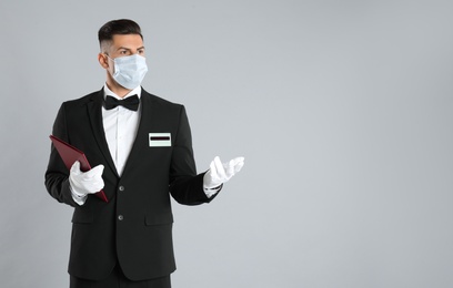 Photo of Waiter in medical face mask with menu on light grey background. Space for text