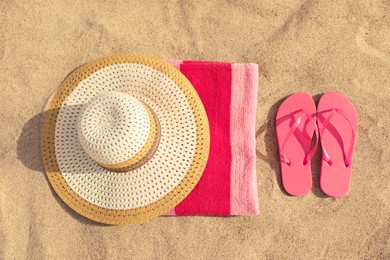 Beach towel with slippers and straw hat on sand, flat lay