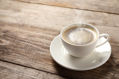 Image of Steaming coffee in cup on wooden table. Space for text