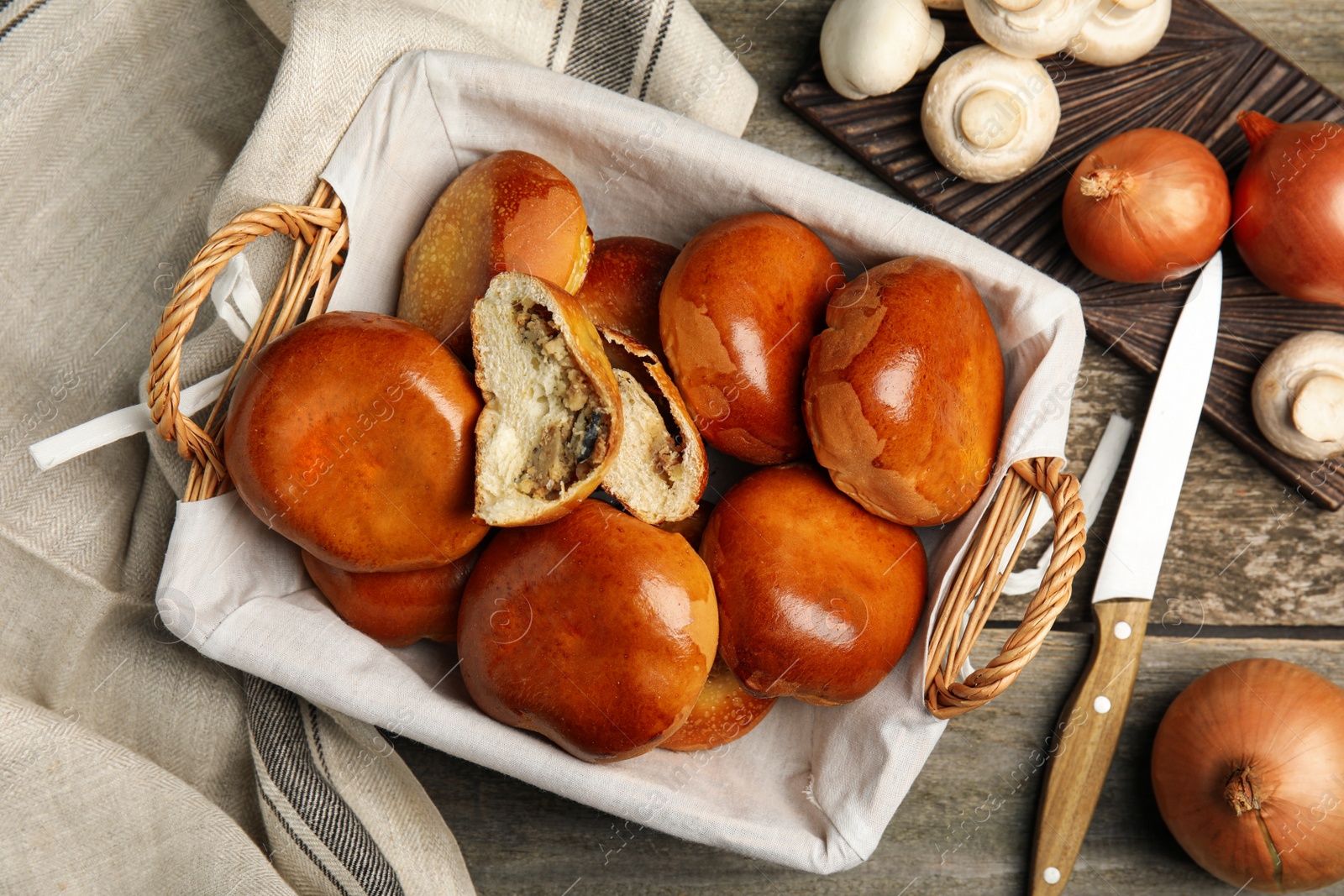 Photo of Wicker basket with delicious baked mushrooms and onion pirozhki on wooden table, flat lay